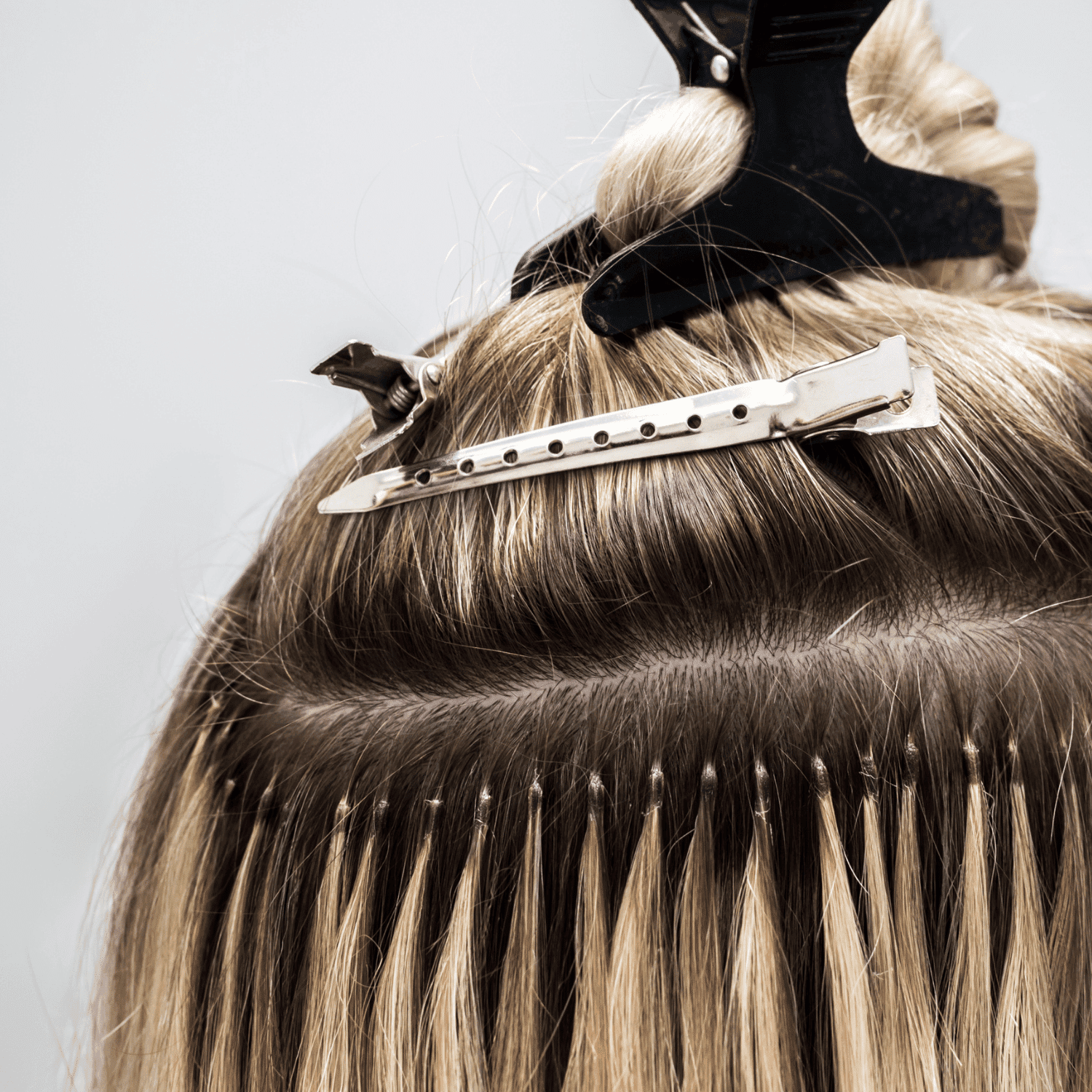 Hair extensions being applied with a metal clip, secured under a top section of hair.
