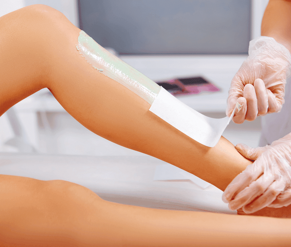 Aesthetician performing wax hair removal on client's leg.