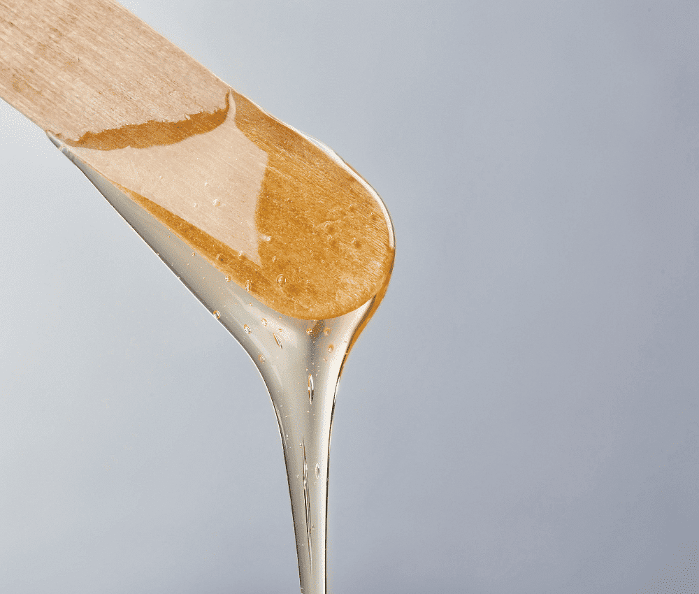 Honey dripping from a wooden dipper against a light background.