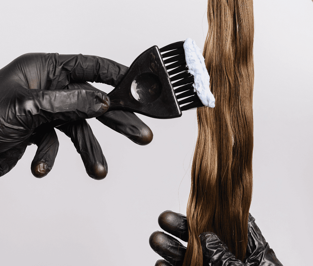 Gloved hands applying hair dye with a brush on long hair.